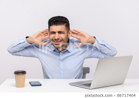 Confused man employee sitting at desk workplace with laptop, holding hands near ears trying to hear better, difficult to listen in noisy office. indoor studio shot isolated on white background 86717404