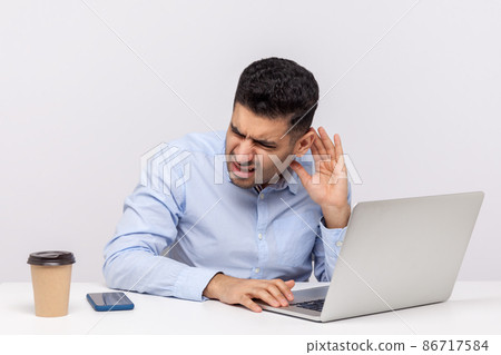 Confused businessman sitting office workplace, leaning towards laptop and holding hand near ear trying to hear better, listening for quiet noise. indoor studio shot isolated on white background 86717584