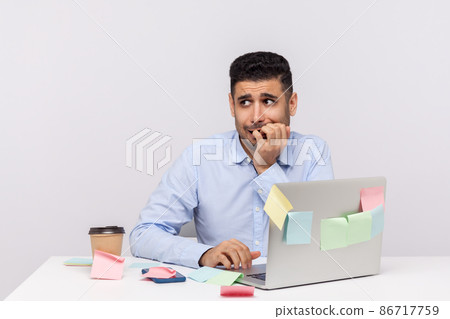 Anxiety disorder, stressful job. Unhappy frustrated man employee sitting in office workplace with sticky notes all around, biting finger nails, nervous about deadline. indoor studio shot isolated Anxiety disorder, stressful job. Unhappy frustrated man employee sitting in office workplace with sticky notes all around, biting finger nails, nervous about deadline. indoor studio shot isolated 86717759