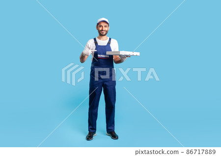Full length positive professional courier in workwear and protective gloves pointing at pizza box, smiling friendly to camera. Fast food delivery service. studio shot isolated on blue background Full length positive professional courier in workwear and protective gloves pointing at pizza box, smiling friendly to camera. Fast food delivery service. studio shot isolated on blue background 86717889