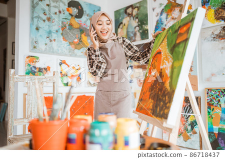 muslim asian female artist painting on canvas and talking to phone 86718437