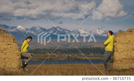 Man and woman in yellow green sportswear. Lovely couple of travelers hug and kiss near old stone enjoying highland landscape. Man and woman in yellow green sportswear. Lovely couple of travelers hug and kiss near old stone enjoying highland landscape. 86718735