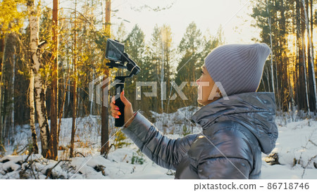 Professional Videographer Holding DSLR Camera on 3-axis Gimbal Stabilization Device in Winter. Cinematographer Operator. Slow Motion Professional Videographer Holding DSLR Camera on 3-axis Gimbal Stabilization Device in Winter. Cinematographer Operator. Slow Motion 86718746
