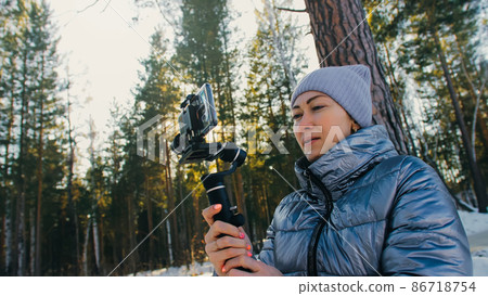 Professional Videographer Holding DSLR Camera on 3-axis Gimbal Stabilization Device in Winter. Cinematographer Operator. Slow Motion Professional Videographer Holding DSLR Camera on 3-axis Gimbal Stabilization Device in Winter. Cinematographer Operator. Slow Motion 86718754