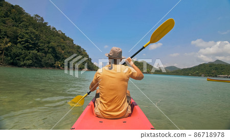 Man with sunglasses and hat rows pink plastic canoe along sea ag 86718978