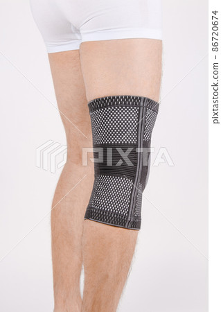Knee Support Brace on leg isolated on white background. Elastic orthopedic orthosis. Anatomic braces for knee fixation, injuries and pain. Protective knee joint bandage sleeve. Trauma, rehabilitation. 86720674