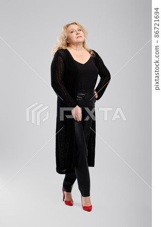 Full body photo of happy old woman in knitted cardigan and faux leather trousers over grey studio background Full body photo of happy old woman in knitted cardigan and faux leather trousers over grey studio background 86721694