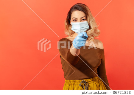 Portrait of strict woman wearing hygienic face mask and gloves, pointing finger to camera, giving recommendations to prevent coronavirus disease, 2019-ncov pandemic threat. indoor studio shot isolated Portrait of strict woman wearing hygienic face mask and gloves, pointing finger to camera, giving recommendations to prevent coronavirus disease, 2019-ncov pandemic threat. indoor studio shot isolated 86721838