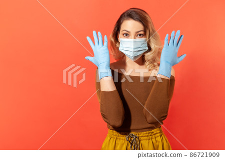 Portrait of woman wearing surgical face mask and gloves to prevent viral disease, coronavirus pandemic threat, 2019-ncov protection recommendations. indoor studio shot isolated on red background 86721909