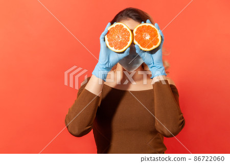 Woman in protective gloves and face mask covering eyes with orange fresh fruits, natural vitamins for immune system and flu treatment, healthy nutrition during quarantine. studio shot, isolated Woman in protective gloves and face mask covering eyes with orange fresh fruits, natural vitamins for immune system and flu treatment, healthy nutrition during quarantine. studio shot, isolated 86722060