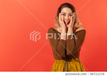 I can't believe. Portrait of happy amazed young woman in casual clothes who were very surprised by good news, victory, triumph and hold head by her arms. Indoor studio shot isolated on red background I can't believe. Portrait of happy amazed young woman in casual clothes who were very surprised by good news, victory, triumph and hold head by her arms. Indoor studio shot isolated on red background 86722216