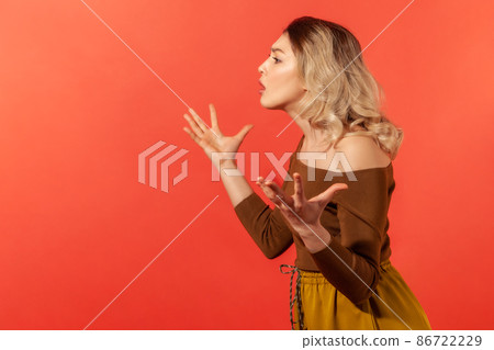 Side view portrait of unhappy and serious woman raised hands with wide fingers spread and demonstrate confusion and misunderstanding of the situation. Indoor studio shot isolated on red background 86722229