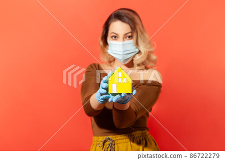 Woman in protective mask and gloves showing paper house on her hand, recommendation to stay home, adhere quarantine while contagious disease spread, coronavirus outbreak. indoor studio shot isolated Woman in protective mask and gloves showing paper house on her hand, recommendation to stay home, adhere quarantine while contagious disease spread, coronavirus outbreak. indoor studio shot isolated 86722279