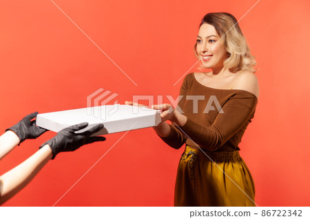 Woman taking pizza from courier hands in protective gloves, safe food delivery on quarantine, coronavirus 2019-ncov prevention. Stay home, order online. indoor studio shot isolated on red background Woman taking pizza from courier hands in protective gloves, safe food delivery on quarantine, coronavirus 2019-ncov prevention. Stay home, order online. indoor studio shot isolated on red background 86722342