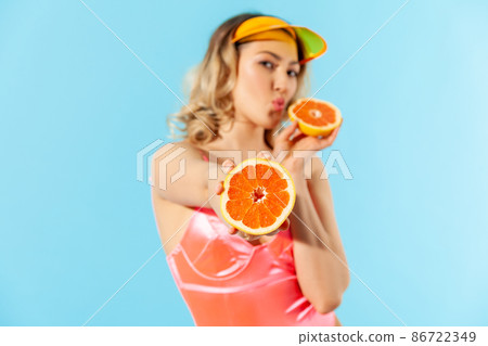 Portrait of beautiful woman in swimsuit giving fresh cut orange to camera and sending air kiss with pout lips. Concept of female beauty, natural healthy nutrition, dietary fruits. studio shot isolated 86722349