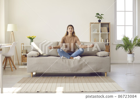 Calm young woman sit on sofa with mudra hands practice yoga meditate at home. Relaxed millennial girl relieve negative emotion breathe fresh air have meditation session. Healthy lifestyle concept. Calm young woman sit on sofa with mudra hands practice yoga meditate at home. Relaxed millennial girl relieve negative emotion breathe fresh air have meditation session. Healthy lifestyle concept. 86723084