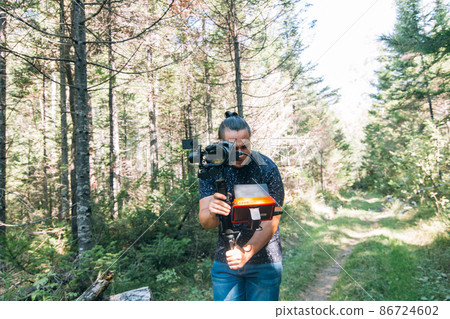 Professional Videographer Holding DSLR Camera on 3-axis Gimbal Stabilization Device in Forest. Cinematographer Operator. Slow Motion 86724602