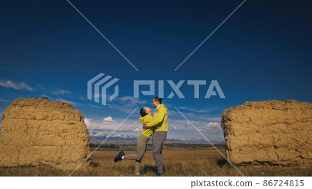 Man and woman in yellow green sportswear. Lovely couple of travelers hug and kiss near old stone enjoying highland landscape. Man and woman in yellow green sportswear. Lovely couple of travelers hug and kiss near old stone enjoying highland landscape. 86724815