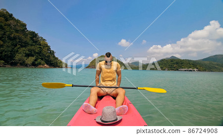 Man with sunglasses and hat rows pink plastic canoe along sea ag 86724908