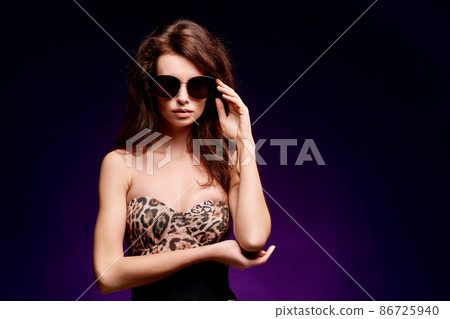 Young sexy woman posing in fashion leopard swimsuit and sunglasses with long hair on dark background 86725940