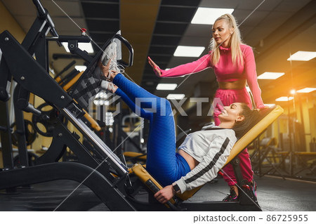 Personal trainer helping woman in works out on training apparatus inside in fitness center. Sporty lifestyle, bodybuilding, training concept 86725955
