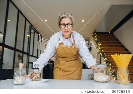 Portrait of strict granny standing in displeased pose staring angry Portrait of strict granny standing in displeased pose staring angry 86726819