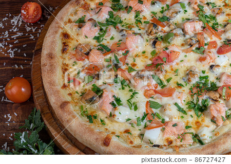 Pizza calzone with bacon and cheese, herbs and cherry tomatoes. With mozzarella, shrimps and octopuses, mussels and other products on a wooden background. 86727427