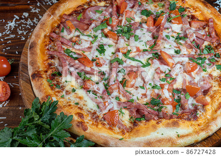 Pizza calzone with bacon and cheese, herbs and cherry tomatoes. With mozzarella, shrimps and octopuses, mussels and other products on a wooden background. 86727428