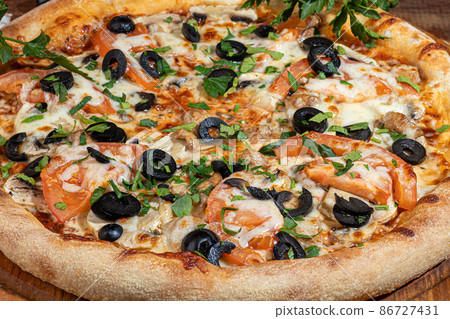 Pizza calzone with bacon and cheese, herbs and cherry tomatoes. With mozzarella, shrimps and octopuses, mussels and other products on a wooden background. 86727431