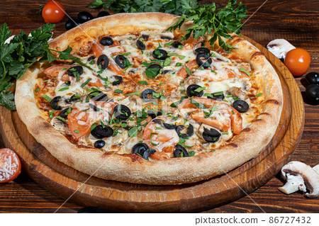 Pizza calzone with bacon and cheese, herbs and cherry tomatoes. With mozzarella, shrimps and octopuses, mussels and other products on a wooden background. 86727432