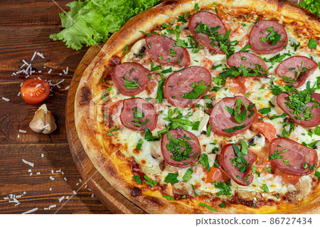 Pizza calzone with bacon and cheese, herbs and cherry tomatoes. With mozzarella, shrimps and octopuses, mussels and other products on a wooden background. 86727434