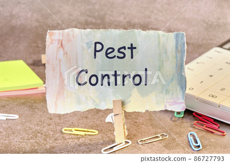 PEST CONTROL phrase written on paper next to scattered paper clips, calculator, adhesive paper 86727793