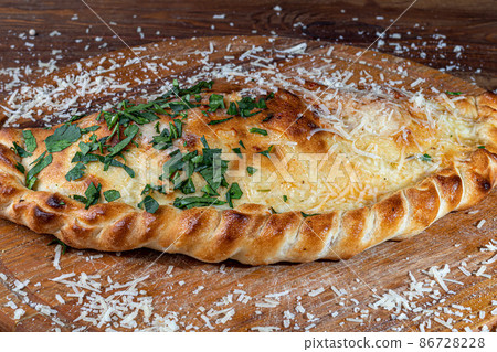 Pizza calzone with bacon and cheese, herbs and cherry tomatoes. With mozzarella, shrimps and octopuses, mussels and other products on a wooden background. Pizza calzone with bacon and cheese, herbs and cherry tomatoes. With mozzarella, shrimps and octopuses, mussels and other products on a wooden background. 86728228