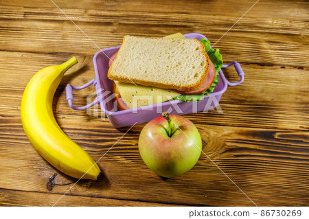 Lunch box with sandwiches, banana and apple on a wooden table 86730269