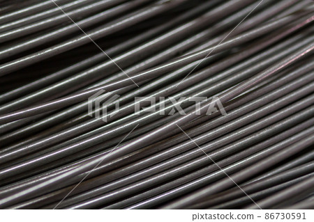Stainless steel wire in production workshop or construction site. Close-up of wire rollers for spring production or concrete reinforcement. Metal texture. Industrial or construction concept. Stainless steel wire in production workshop or construction site. Close-up of wire rollers for spring production or concrete reinforcement. Metal texture. Industrial or construction concept. 86730591