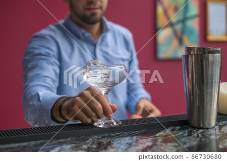 Bartender cools the glass with ice before making a cocktail. Close up photo, process, bar. High quality photo Bartender cools the glass with ice before making a cocktail. Close up photo, process, bar. High quality photo 86730680