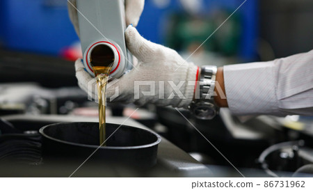 Auto mechanic in gloves pour engine oil into engine 86731962
