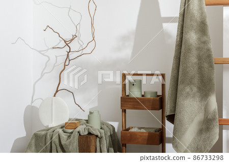 Modern aesthetic bathroom accessories in eucalyptus light  green shade. Organic cotton bath towels, minimalistic Scandinavian style vase, sensor soap and lotion dispenser  on solid oak stump. Daily 86733298