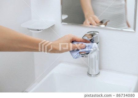 Cleaning the sink faucet with a microfiber cloth. Cleaning the bathroom. Sanitize surfaces prevention in hospital and public spaces against corona virus. Woman hand using wet wipe. 86734080