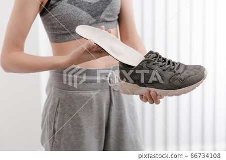 Fitness woman in sportswear with orthopedic insoles and sneakers. Woman putting orthopedic insole into shoe at home close up. Foot care banner. Flat Feet Correction. Fitness woman in sportswear with orthopedic insoles and sneakers. Woman putting orthopedic insole into shoe at home close up. Foot care banner. Flat Feet Correction. 86734108