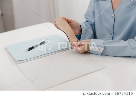 Doctor holding an insole while sitting at a table. Orthopedist tests the medical device. Orthopedic insoles. Foot care. Flat Feet Correction. Treatment and prevention of flat feet and foot diseases. 86734119