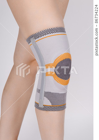 Knee Support Brace on leg isolated on white background. Elastic orthopedic orthosis. Anatomic braces for knee fixation, injuries and pain. Protective knee joint bandage sleeve. Trauma, rehabilitation. 86734224
