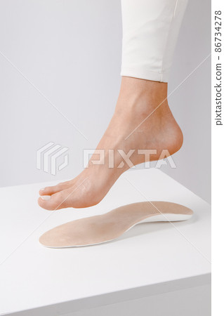 Medical insoles. Isolated orthopedic insoles on a white background. Treatment and prevention of flat feet and foot diseases. Foot care. Insole cutaway layers. Leg hanging over the insole. 86734278