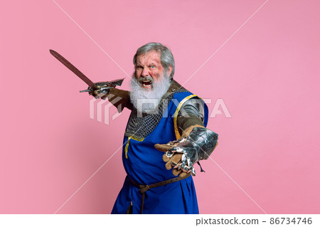 Portrait of senior grey bearded man, brave medieval warrior or knight in armored clothes with sword isolated on pink background. Comparison of eras, history, festival Portrait of senior grey bearded man, brave medieval warrior or knight in armored clothes with sword isolated on pink background. Comparison of eras, history, festival 86734746