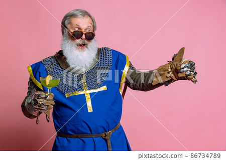 Portrait of senior grey bearded man, brave medieval warrior or knight in armored clothes with sword isolated on pink background. Comparison of eras, history, festival Portrait of senior grey bearded man, brave medieval warrior or knight in armored clothes with sword isolated on pink background. Comparison of eras, history, festival 86734789