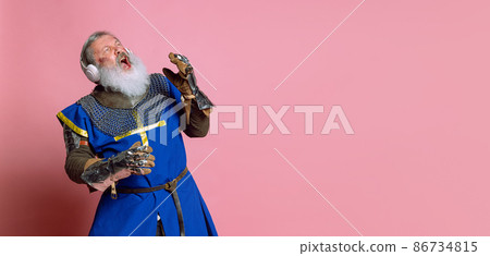 Senior grey bearded man, brave medieval warrior or knight in armored clothes with sword isolated on pink background. Comparison of eras, history, festival Senior grey bearded man, brave medieval warrior or knight in armored clothes with sword isolated on pink background. Comparison of eras, history, festival 86734815