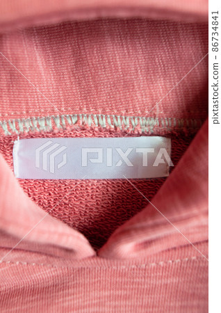 Closeup white blank clothing tag label on pink collar hoodie. Vertical photo. Selective focus. Closeup white blank clothing tag label on pink collar hoodie. Vertical photo. Selective focus. 86734841