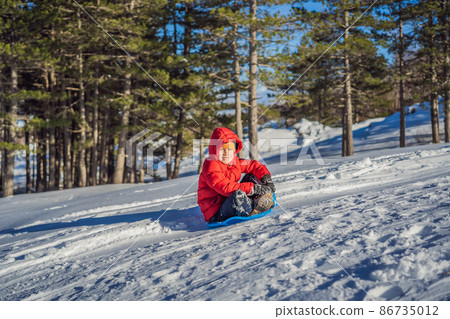 happy and positive little boy enjoying sledding and cold weather outdoor, winter fun activity concept 86735012