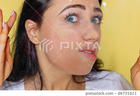 Close-up face of shocked young girl crushed on glass isolated on yellow studio background. Concept of human emotions, facial expression, youth. 86735821