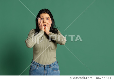 Surprised young beautiful girl wearing olive color sweatshirt isolated on green background. Concept of emotions, facial expression Surprised young beautiful girl wearing olive color sweatshirt isolated on green background. Concept of emotions, facial expression 86735844
